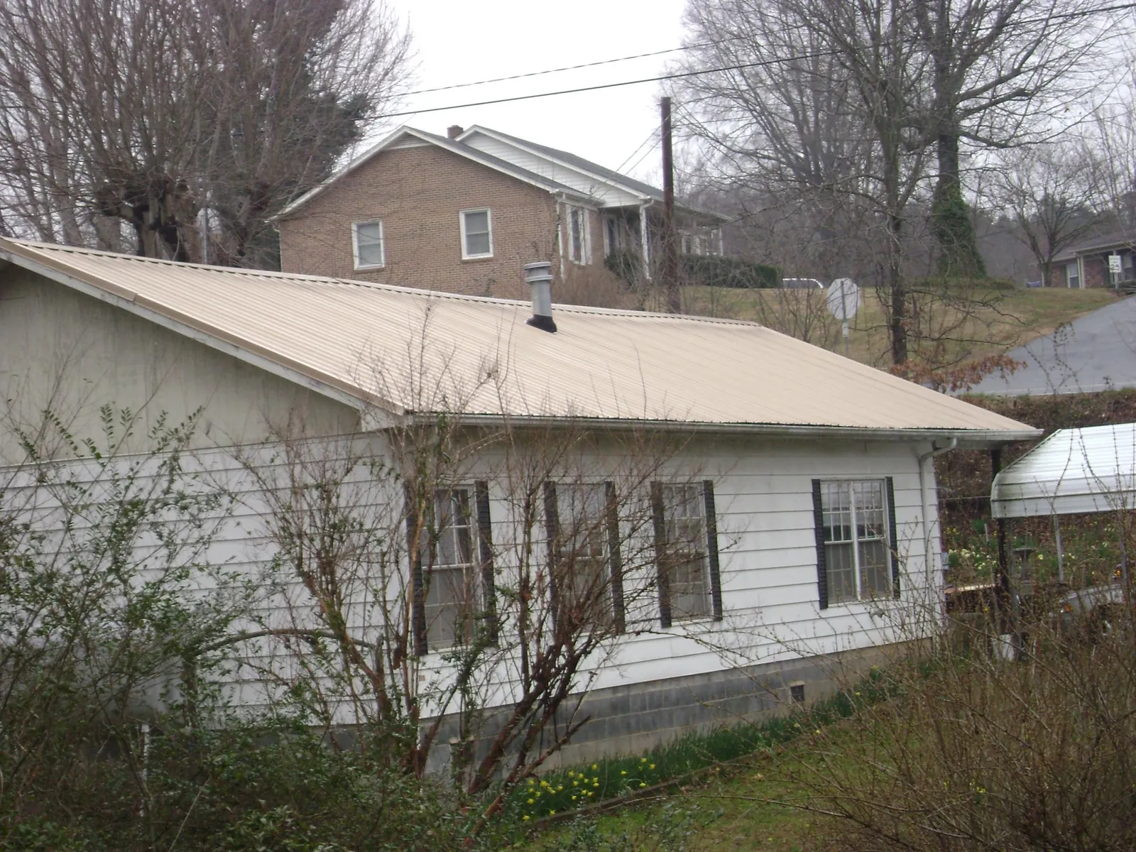 Tan metal roof on a white sided house set into a hillside — Commercial Roofing by Roofing Brothers in Vienna